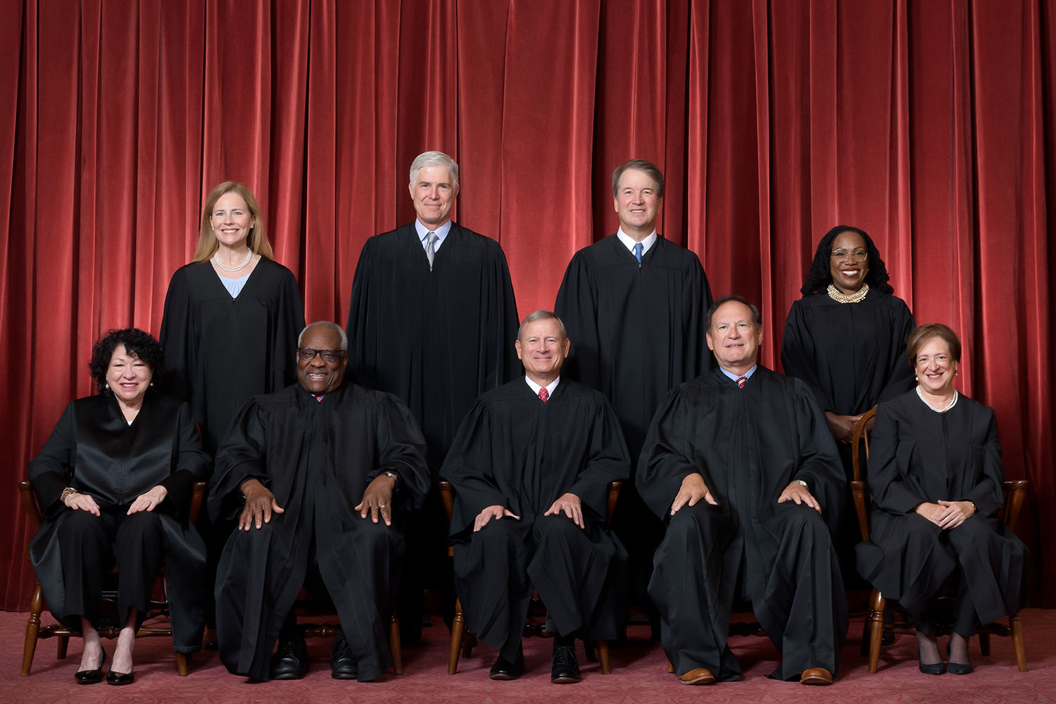 The nine justices of the Supreme Court of the United States in their formal group portrait, seated and standing in front of red curtains